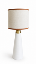 Candeeiro de mesa com base branca de linhas elegantes e detalhe dourado, combinado com abajour em linho natural.